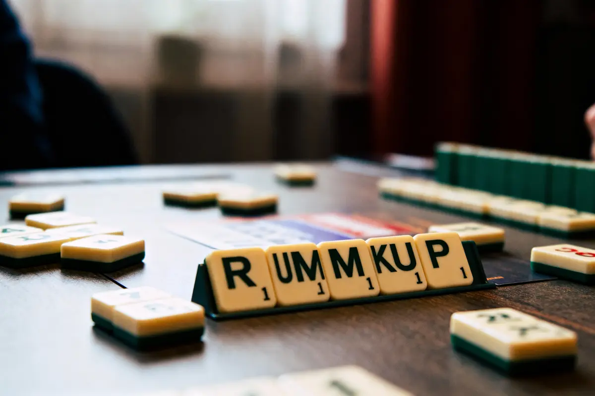 Lettres du jeu Rummikub alignées sur un support de table, pièces dispersées autour.