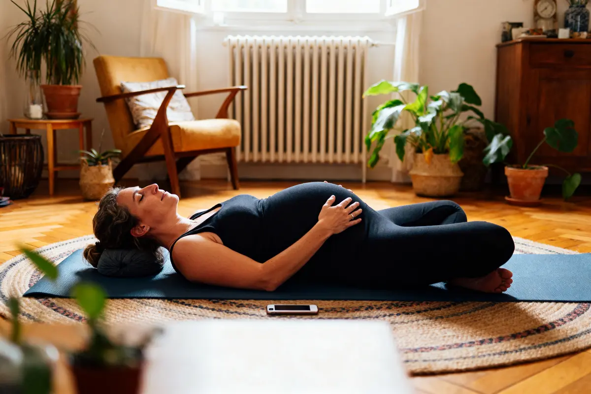Femme enceinte allongée sur un tapis de yoga dans un salon cozy, environné de plantes.