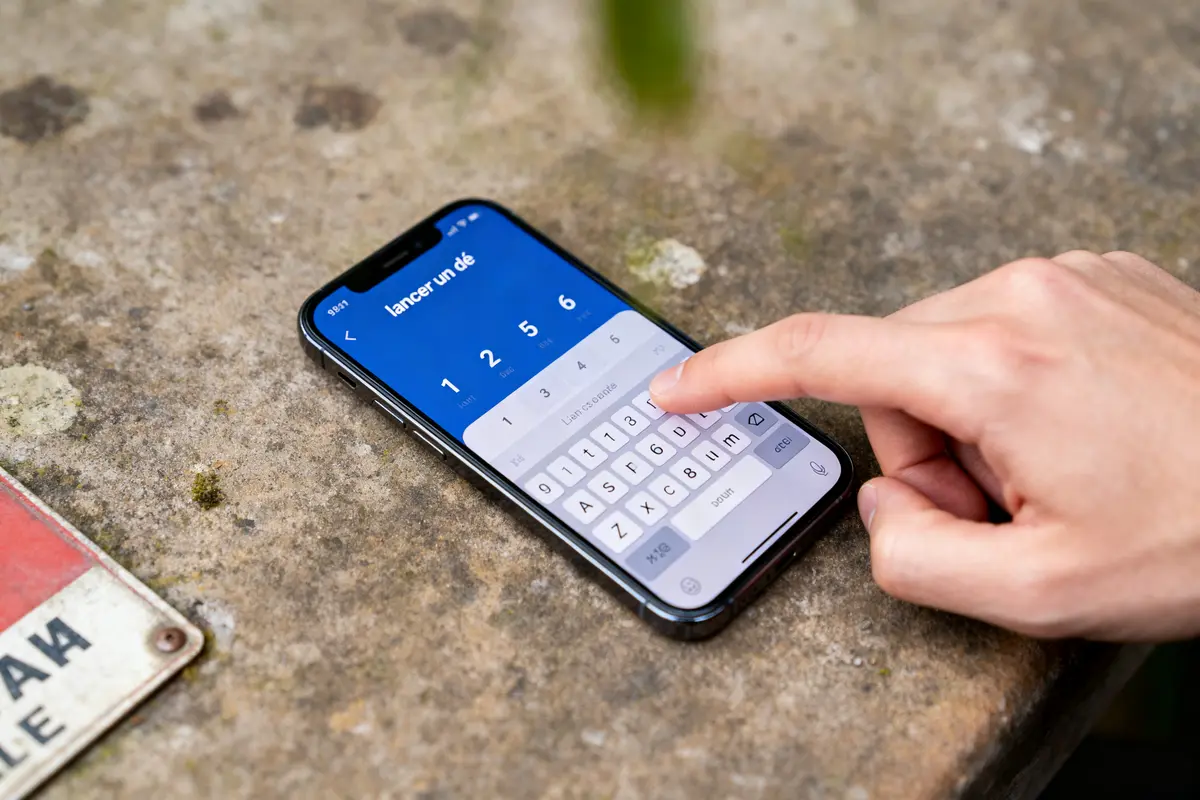 Une main utilise une application de lancer de dé sur un smartphone posé sur une surface rocheuse.