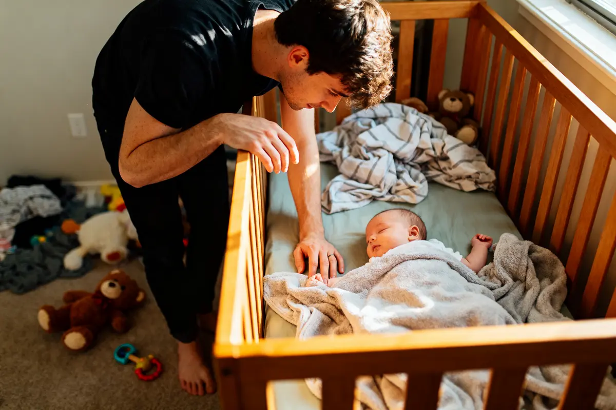 Un adulte surveille un bébé qui dort paisiblement dans un lit d'enfant en bois.