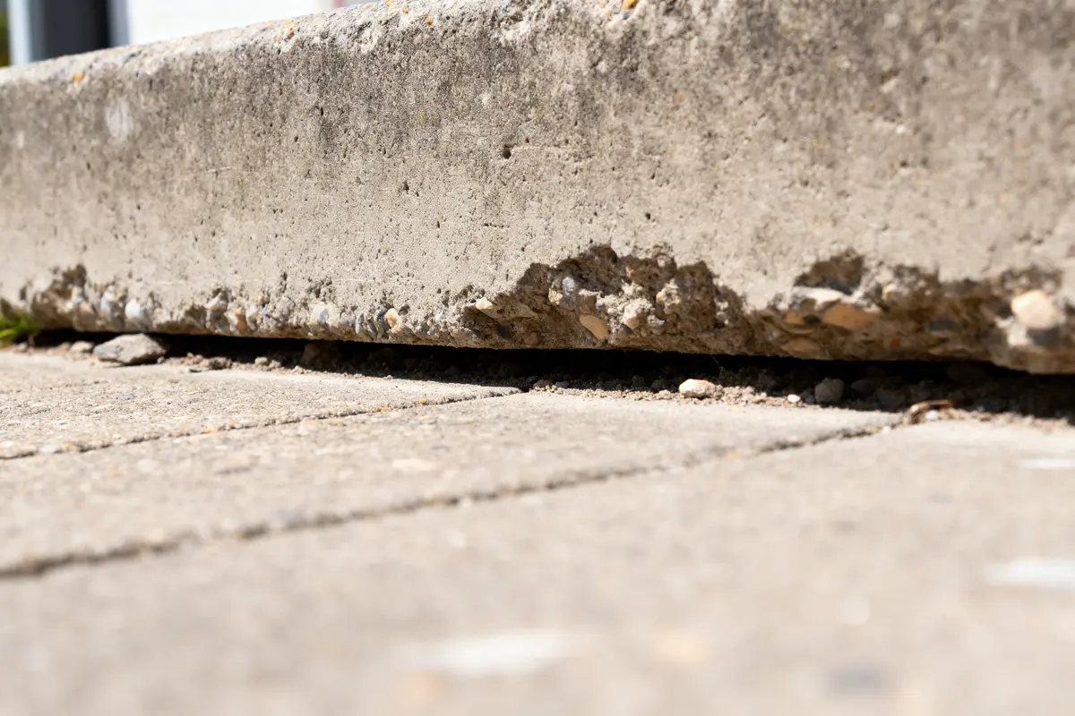 Détail d'une dalle en béton usée avec érosion visible sur le bord inférieur.