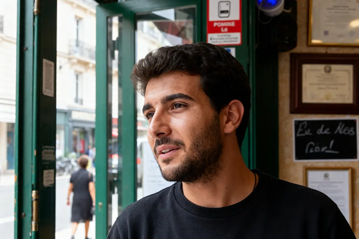 Je vous transmets l’image d’un homme souriant à l’intérieur d’un café parisien