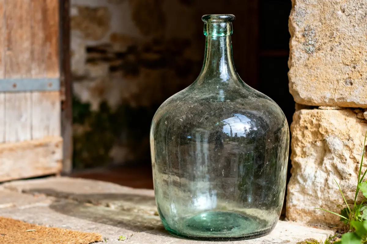 Grande dame-jeanne en verre transparent posée près d'une porte en pierre ancienne