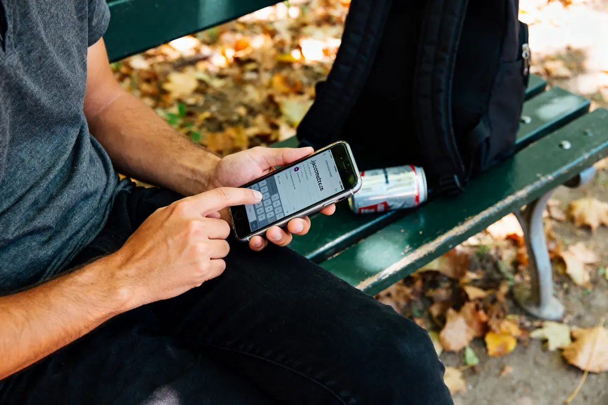 Personne utilisant le site jecontacte.com sur smartphone, assise sur un banc extérieur