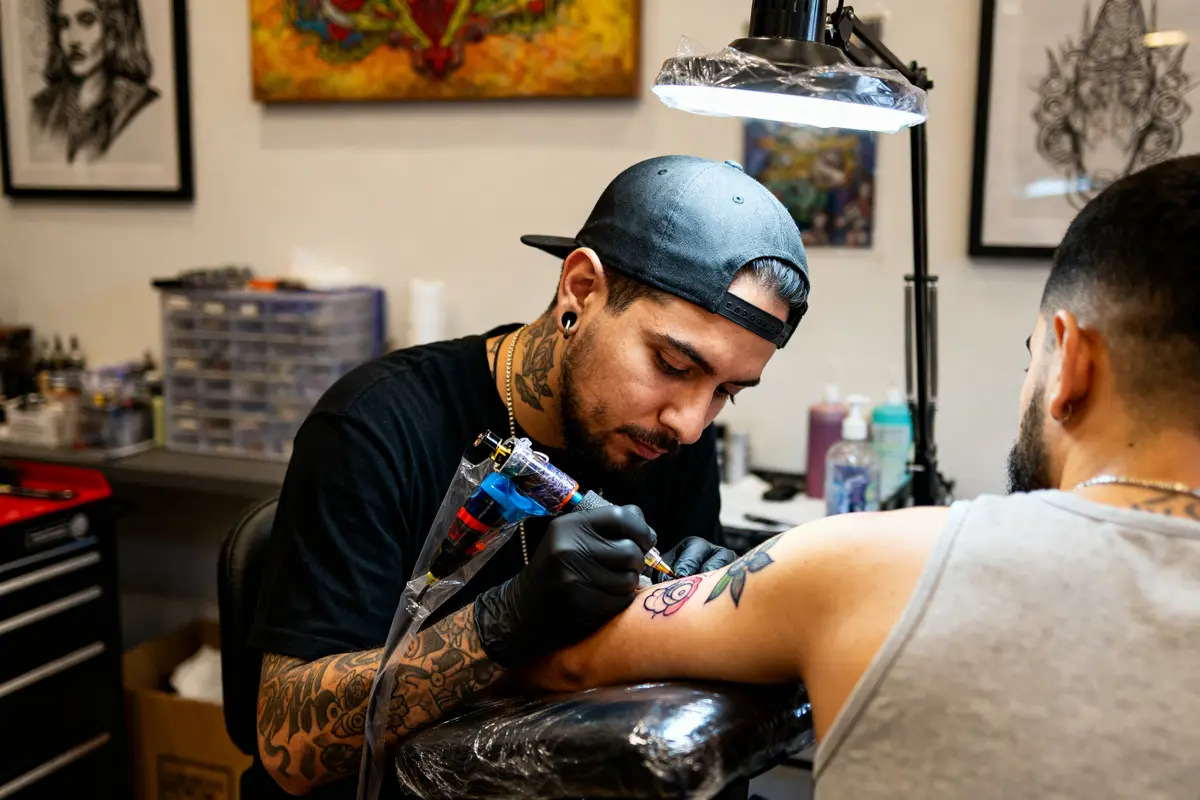 Tatoueur créant un motif floral sur bras, symbolisant le prix d'un tatouage personnalisé.