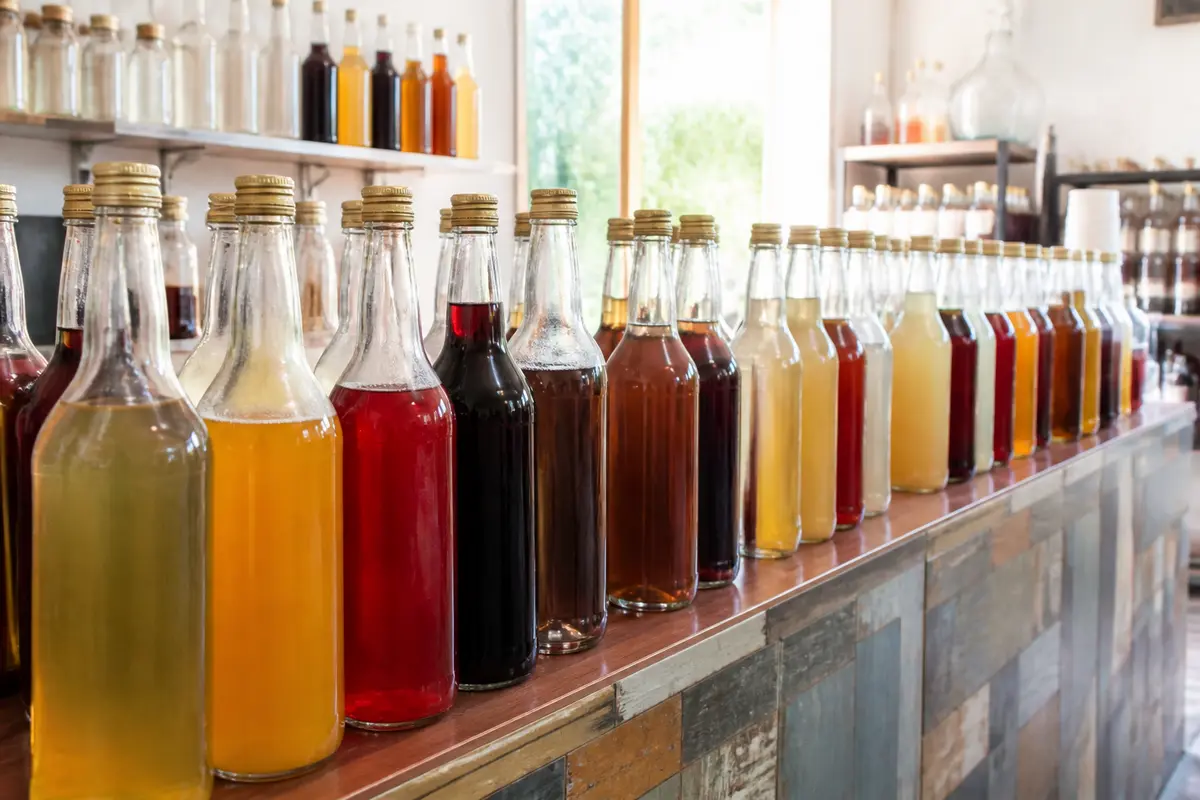 Alignement de bouteilles colorées dans un bar à sirop artisanal au décor vintage